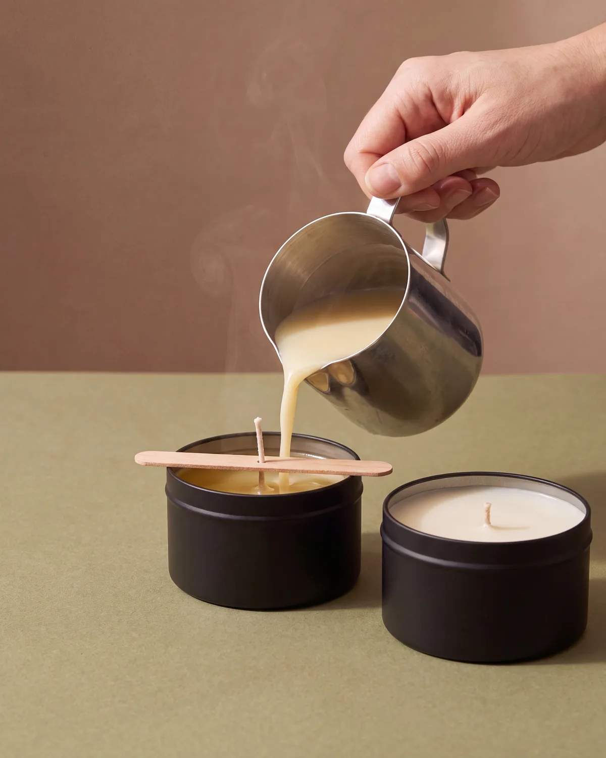 Wax being hand-poured into black candle tins in the studio